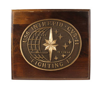 Brown wooden plaque with central oval bronze medallion with USS Intrepid insignia