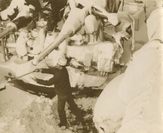 Black and white photograph of a sailor shoveling snow off an anti-aircraft gun mount