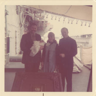 Printed color photograph of two men and a woman posing with a baby on USS Intrepid