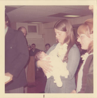 Printed color photograph of a woman holding a baby at a baptism on board Intrepid
