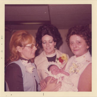 Printed color photograph of three women and a baby in a baptismal outfit