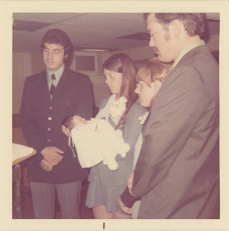 Printed color photograph of two men, two women and a baby at a baptism on board USS Intrepid