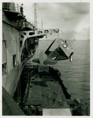 Black and white photograph of an aircraft being hoisted up to USS Intrepid's flight deck