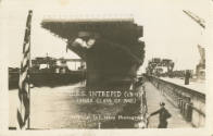 Printed postcard with a black and white photograph of USS Intrepid docked in port