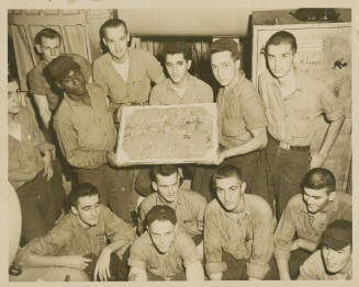 Printed black and white photograph of a group of USS Intrepid crewmembers holding a cake in a s…