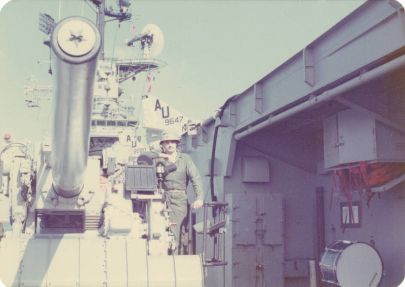 Color photograph of George Mehlig, a U.S. Marine, posing on a gun mount on USS Intrepid