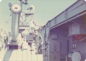 Color photograph of George Mehlig, a U.S. Marine, posing on a gun mount on USS Intrepid