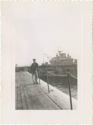 Black and white photograph of a sailor posing with USS Hornet in background