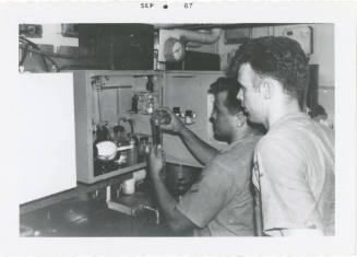 Black and white photograph of two crew members in the oil and water testing lab