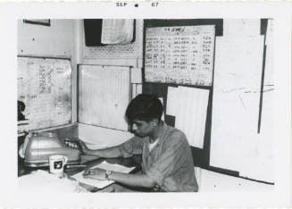 Black and white photograph of a crew member working at a desk in the B Division office