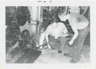 Back and white photograph of two crew members lighting a boiler in a ship's fire room