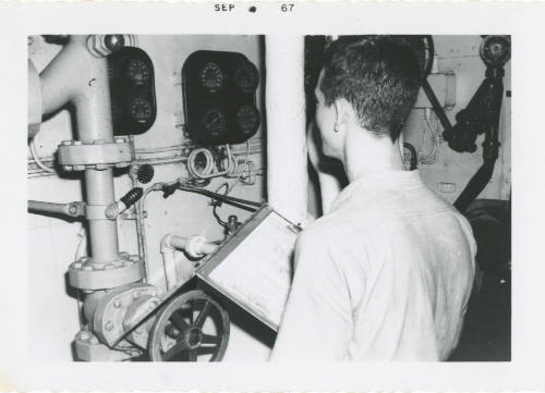 Black and white photograph of a crew member taking readings in a fire room
