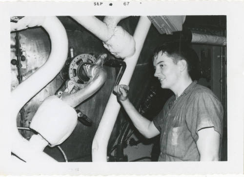 Black and white photograph of a crew member operating a soot blower in a ship's fire room