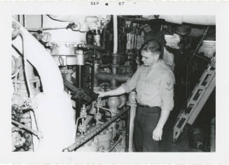 Black and white photograph of a crew member at the emergency feed pump in a ship's fire room