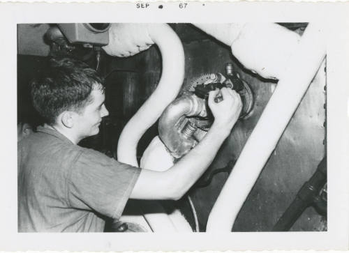 Black and white photograph of a crew member operating a soot blower in a ship's fire room