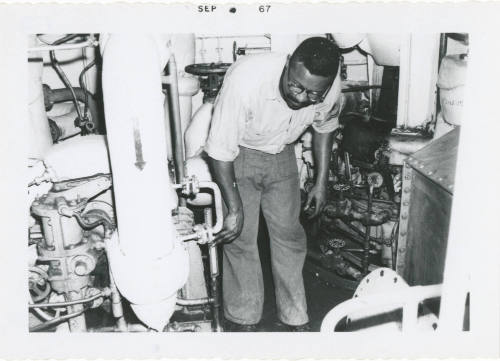 Black and white photograph of a crew member inspecting a fire pump