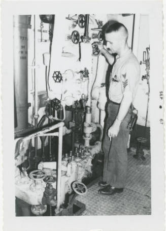 Black and white photograph of a crew member adjusting a valve in a fire room