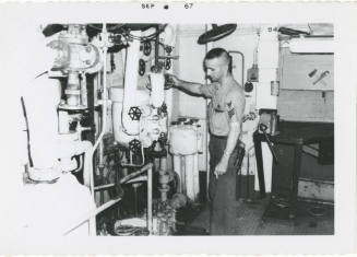 Black and white photograph of a crew member adjusting a valve in a fire room