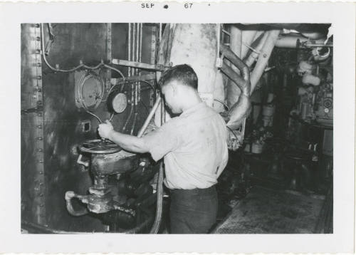 Black and white photograph of a crew member adjusting the main steam stop valve wheel in a fire…