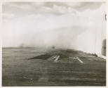 Black and white photograph of the aircraft carrier USS Intrepid's flight deck with a wave crest…