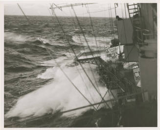 Black and white photograph of waves crashing agains the starboard side of USS Intrepid, with th…