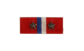 Ribbon bar with red background and blue and white stripes in the center, and bronze stars on ei…