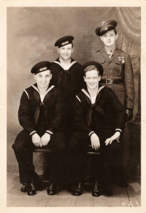 Printed black and white photograph of four men with three wearing U.S. Navy uniforms and one we…